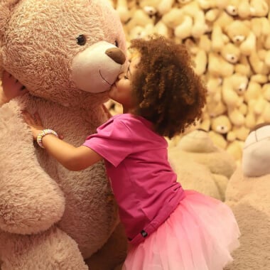 Een klein meisje kust een enorme teddybeer